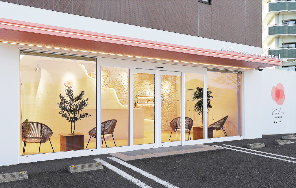 「rota HAIR & EYE coral」の外観。ガラス張りの入り口からは、ナチュラルなインテリアと観葉植物が見える。白とベージュを基調としたデザインで、壁にはサロンのロゴと柔らかな照明が映える。