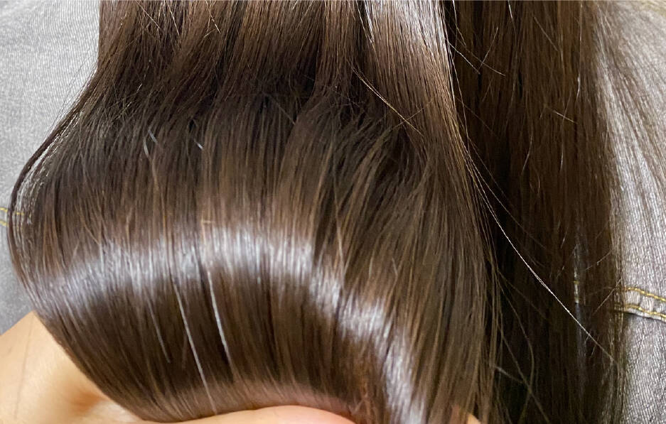 手で束ねられたツヤのあるストレートな髪のクローズアップ。髪の美しさと健康的な輝きが際立っている。