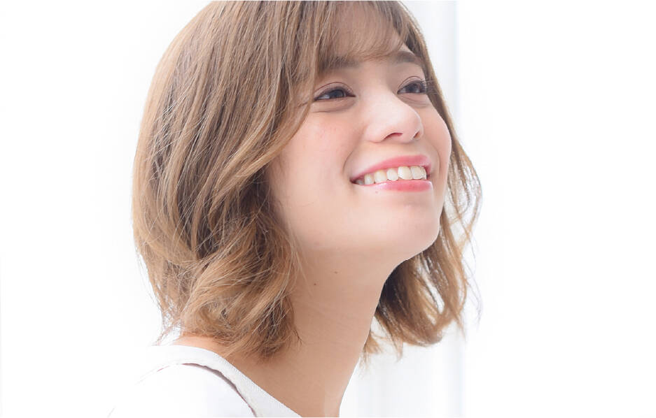 明るい茶色のショートヘアの若い女性が、柔らかい笑顔で横を向いている。自然光が差し込む背景が爽やかな印象を与えている。