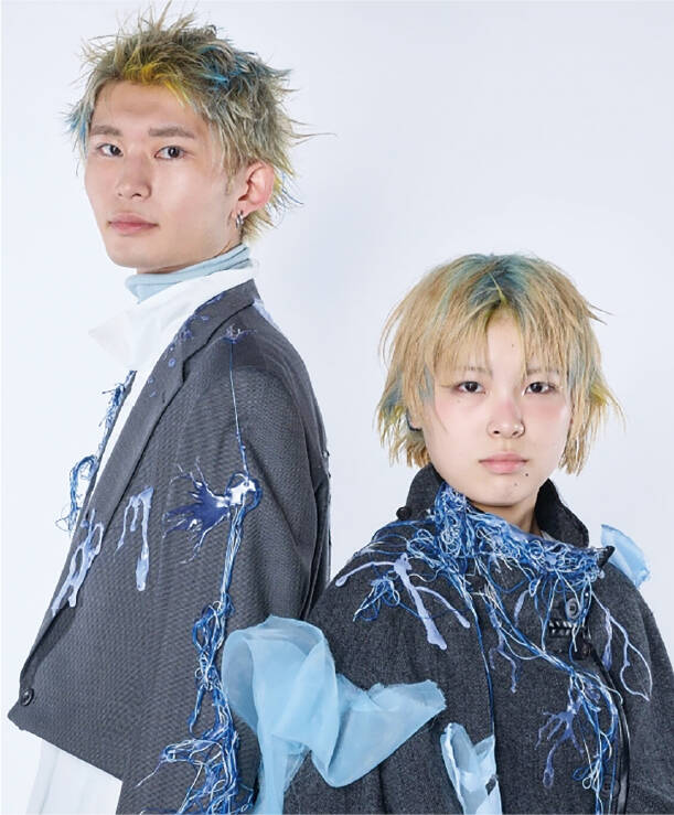 青とゴールドをミックスしたショートヘアを施した2人組が、糸や布素材を大胆にあしらったアート性の高い衣装を身にまとい、独創的な世界観を演出している。